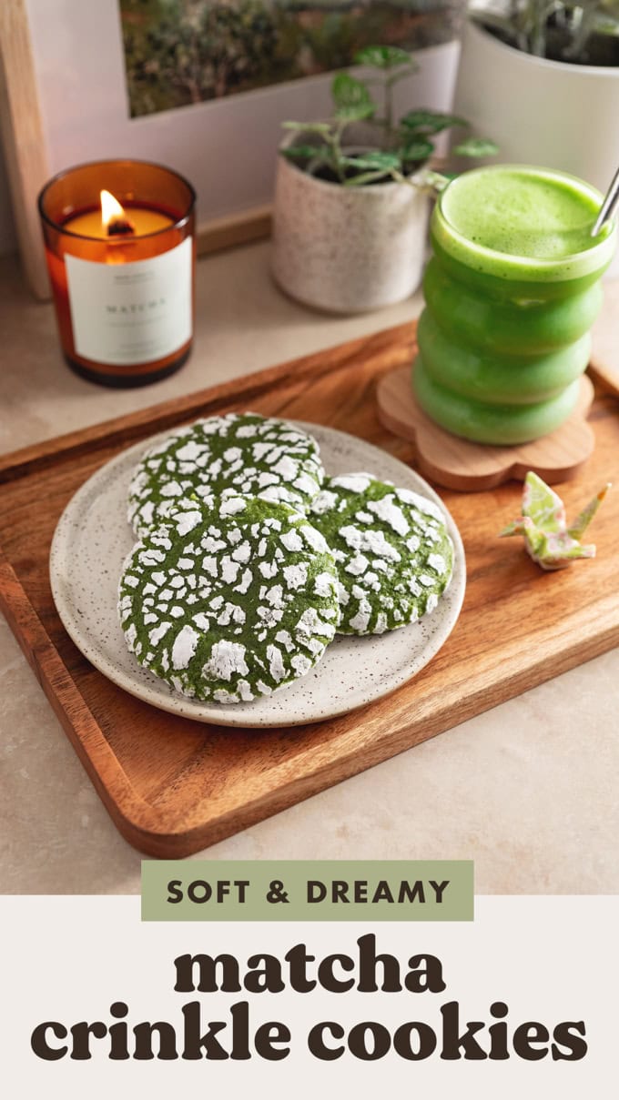 Three matcha crinkle cookies on a wooden platter with a glass of matcha latte next to it.