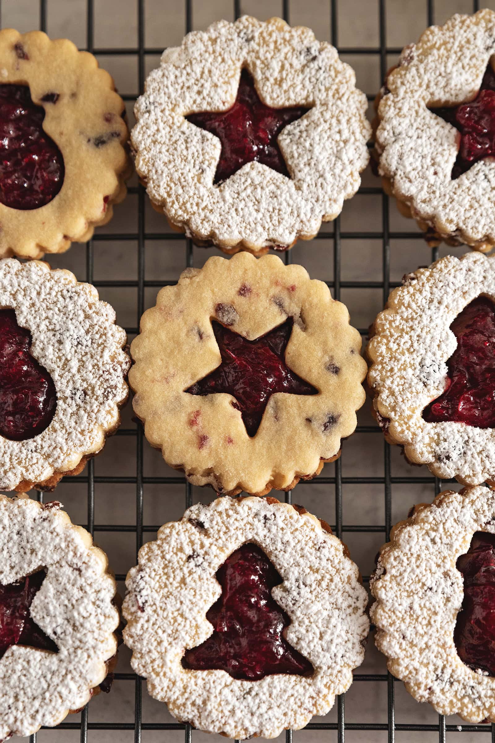 Overhead view of cranberry linzer cookies lined up on a wire rack with various holiday cut-outs.