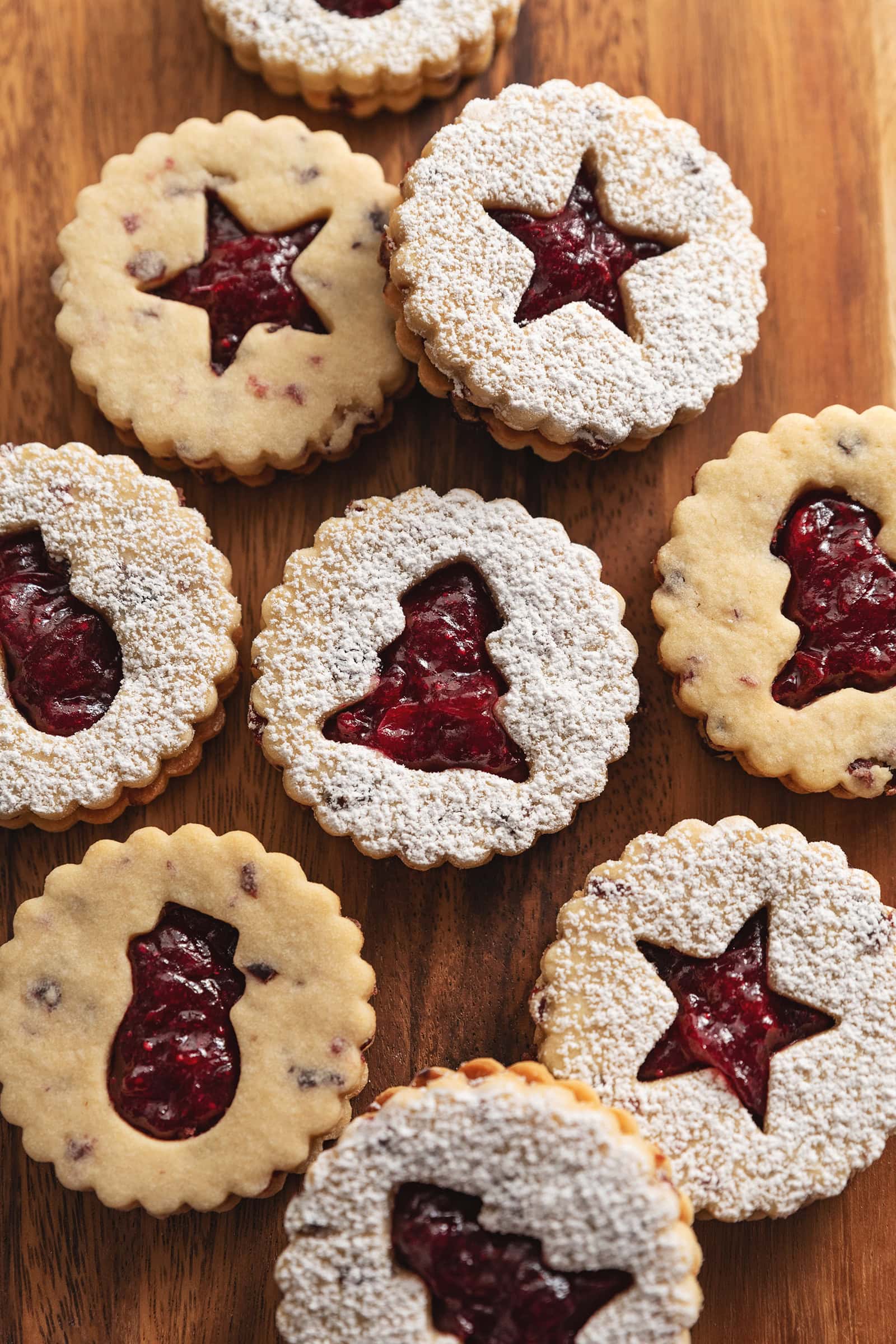 Cranberry linzer cookies with various holiday-shaped cut-outs on a wooden board.