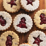 Cranberry linzer cookies with various holiday-shaped cut-outs on a wooden board.