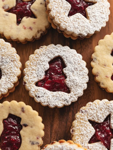 Cranberry linzer cookies with various holiday-shaped cut-outs on a wooden board.
