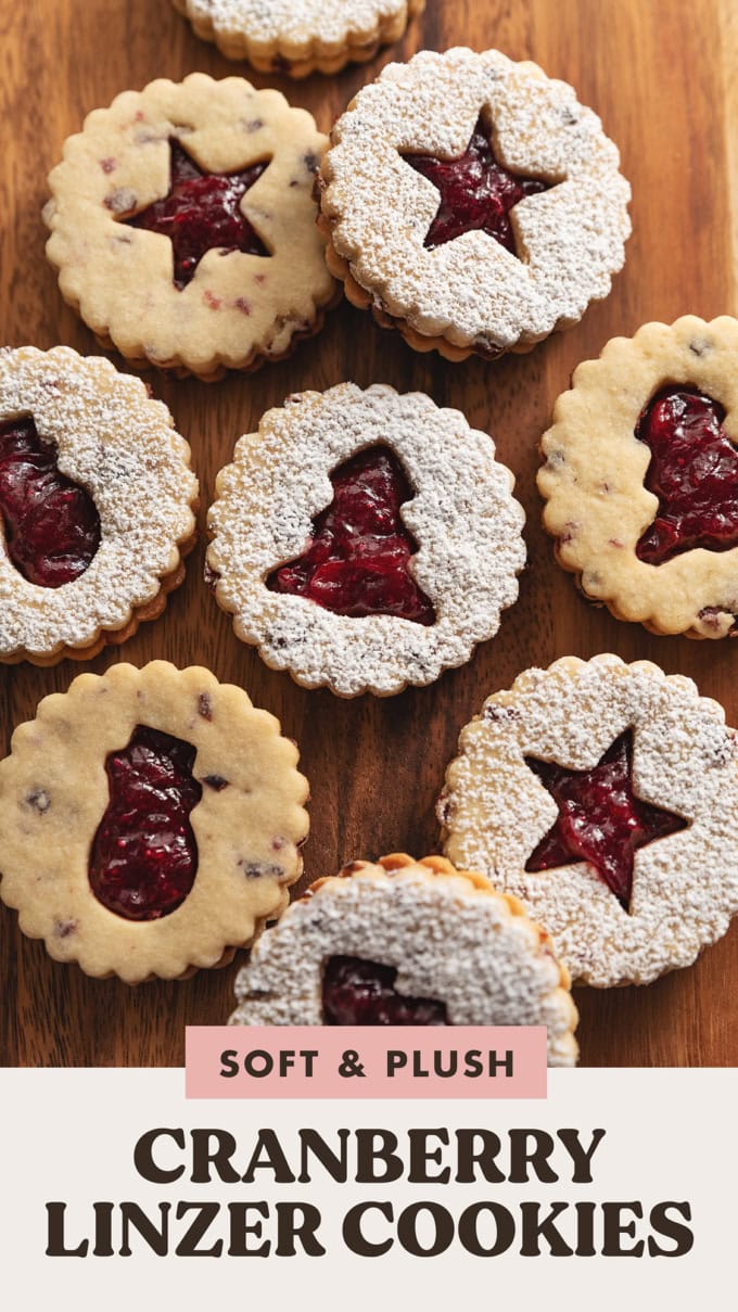 Cranberry linzer cookies with various holiday-shaped cut-outs on a wooden board.