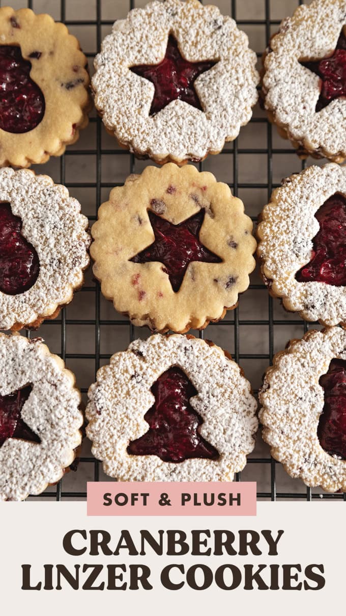 Overhead view of cranberry linzer cookies lined up on a wire rack with various holiday cut-outs.