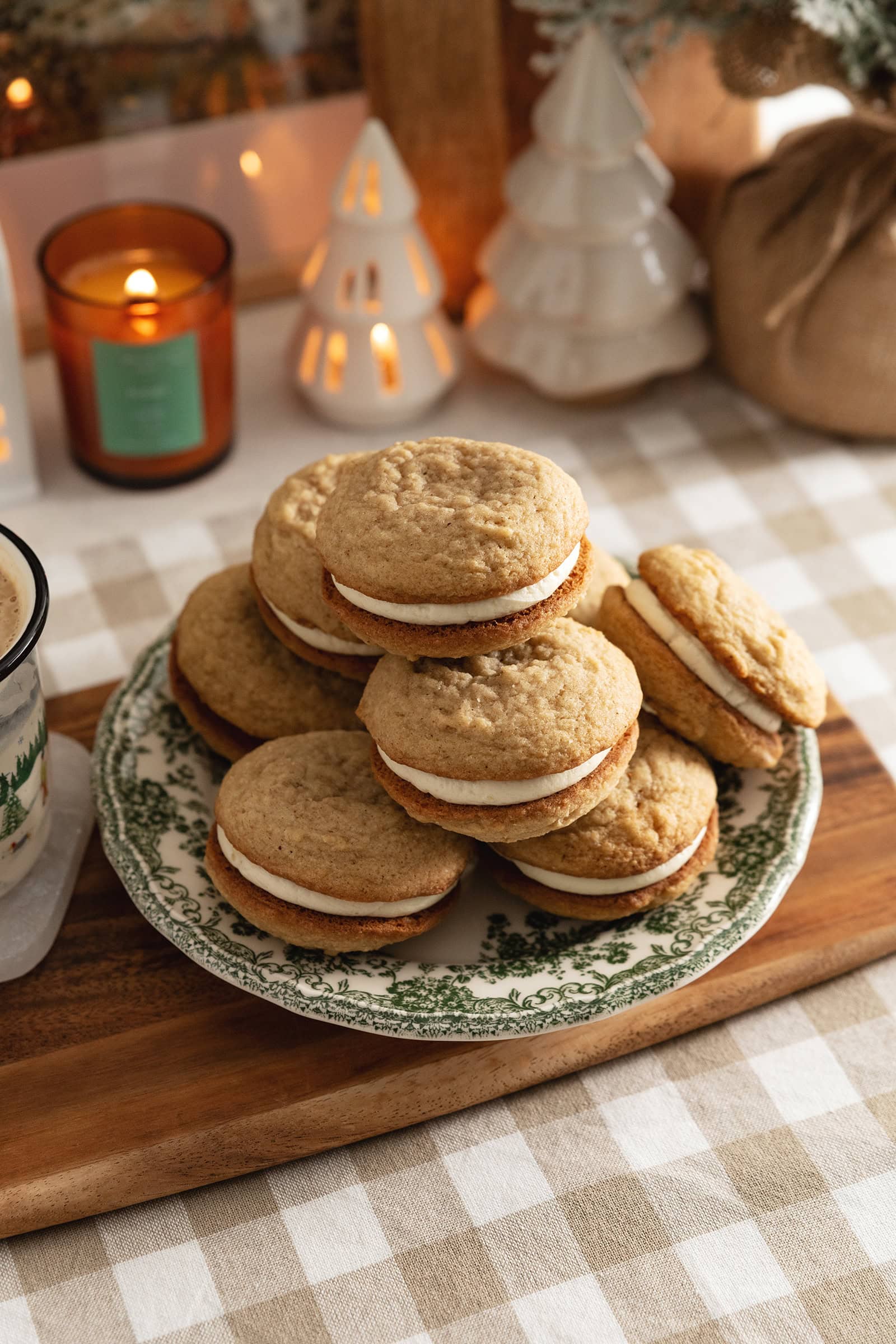 Eggnog sandwich cookies piled up on a plate on a kitchen counter.
