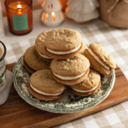 Eggnog sandwich cookies piled up on a plate on a kitchen counter.