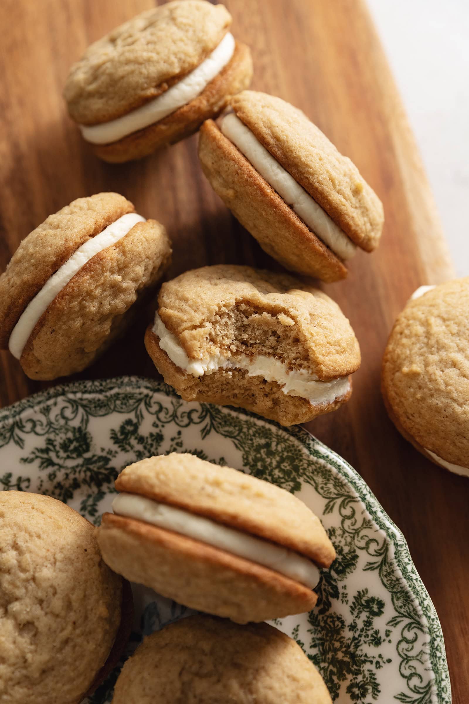 Eggnog sandwich cookies scattered on a wooden board with a bite taken out of one of the cookies.