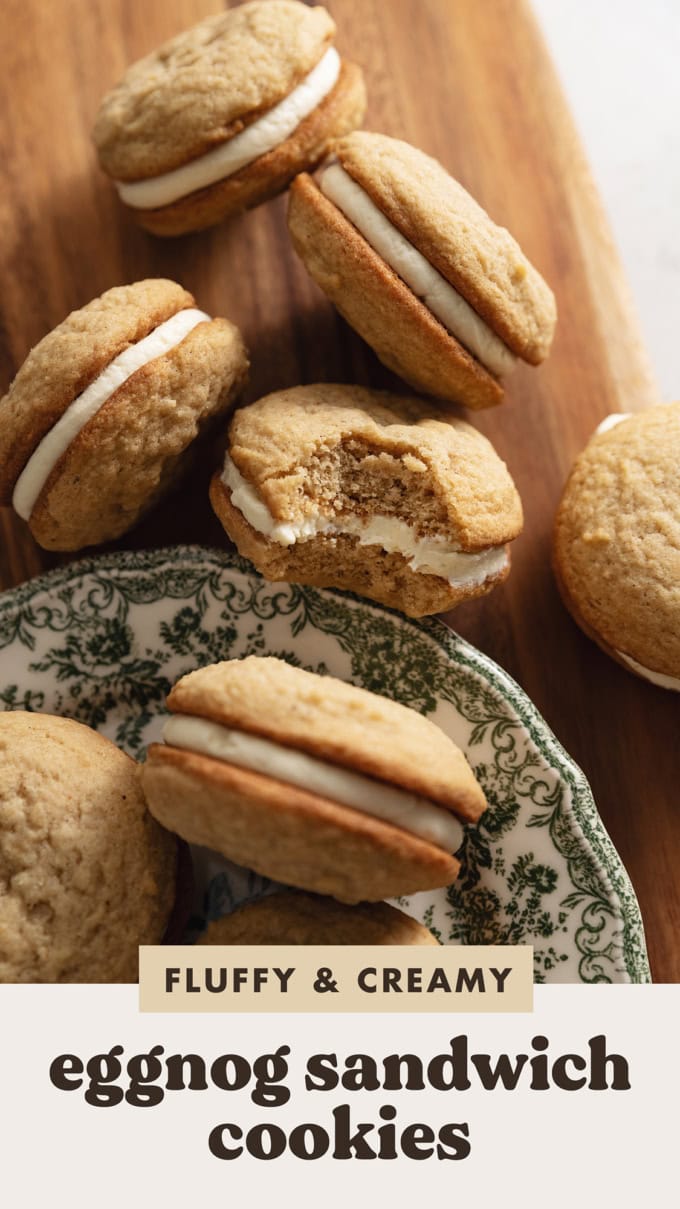 Eggnog sandwich cookies scattered on a wooden board with a bite taken out of one of the cookies.