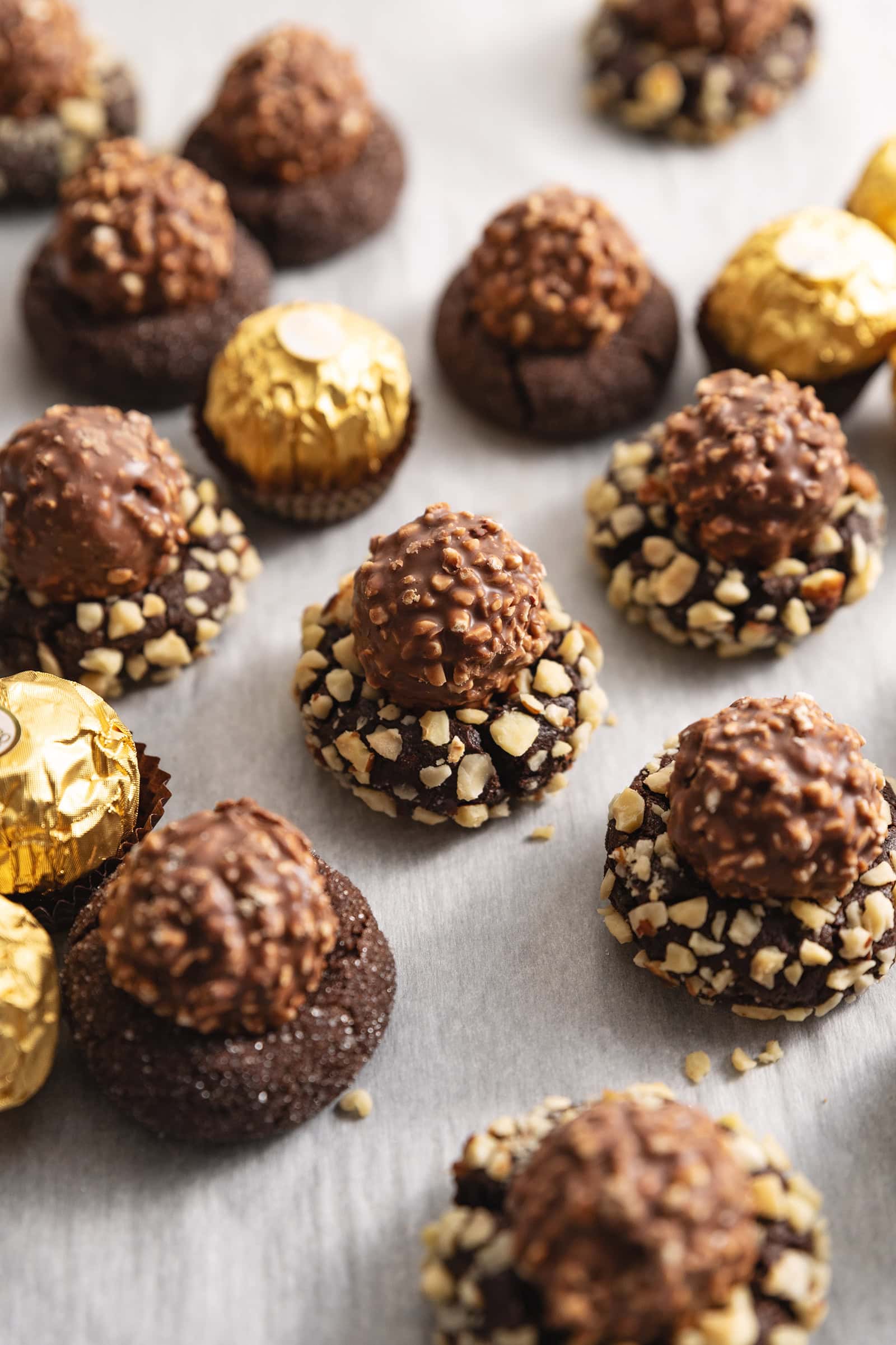 Ferrero rocher blossom cookies scattered on parchment paper with wrapped chocolates around them.