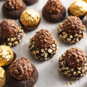 Ferrero rocher blossom cookies scattered on parchment paper with wrapped chocolates around them.