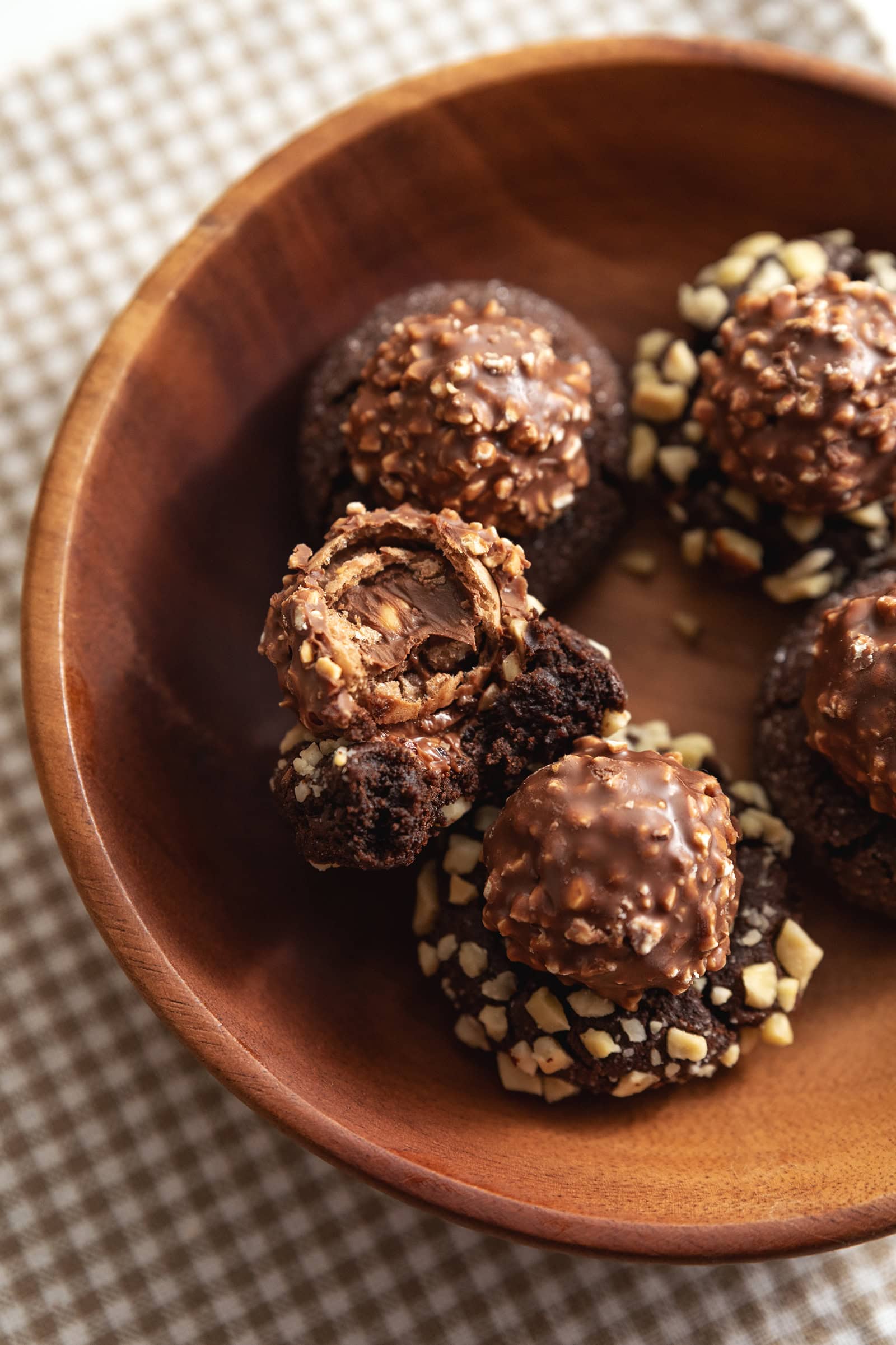 A ferrero rocher blossom cookie with a bite taken out of it in a wooden bowl.