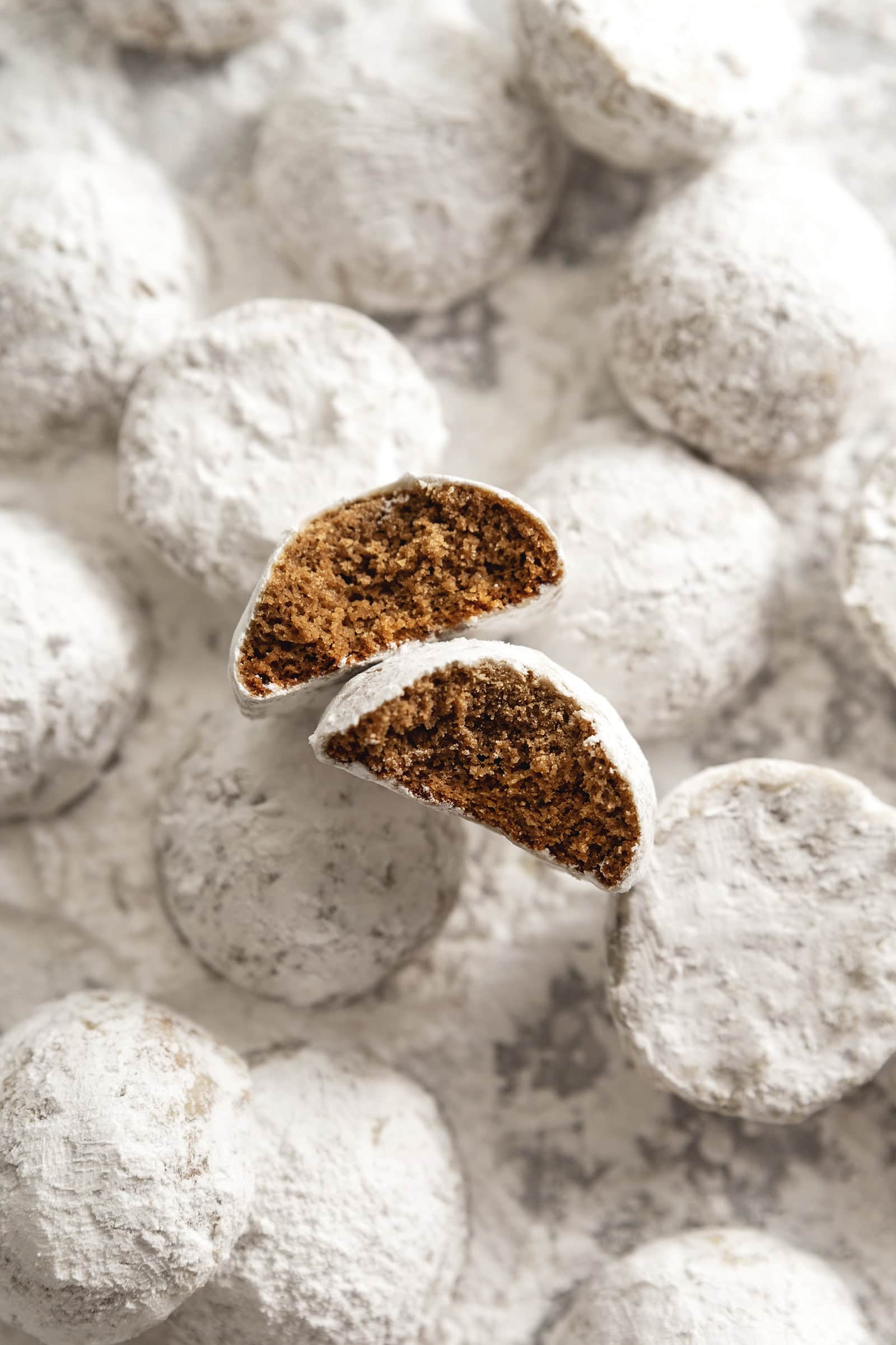 Two hojicha snowball cookies with bites taken out of them among several other cookies dusted with powdered sugar.