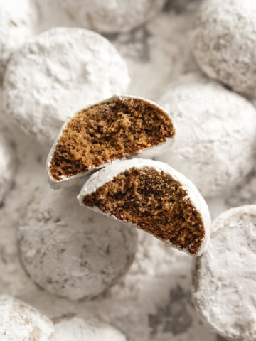 Two hojicha snowball cookies with bites taken out of them among several other cookies dusted with powdered sugar.