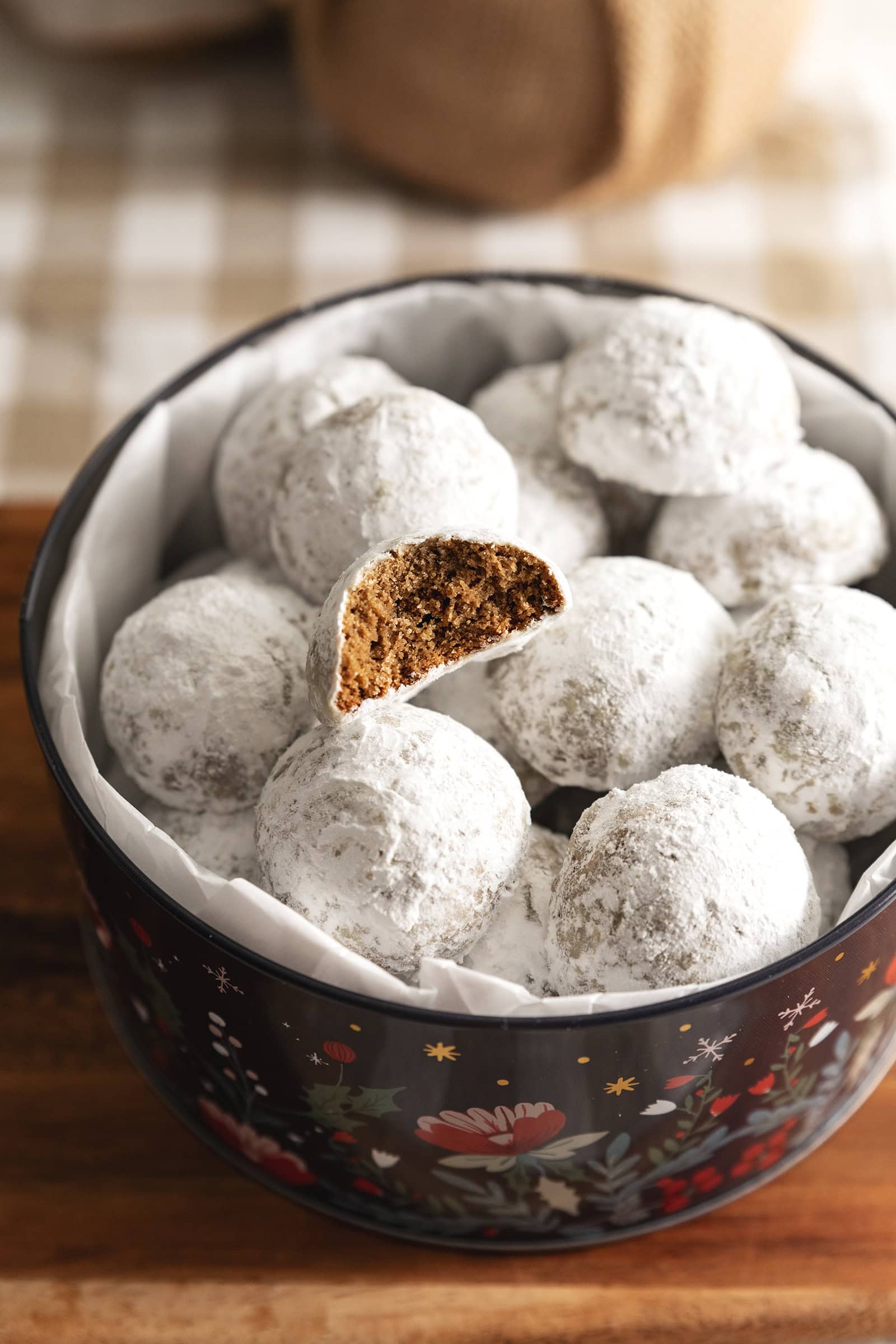 Hojicha snowball cookies in a cookie tin with one cookie on top that has a bite taken out of it to show the texture inside.