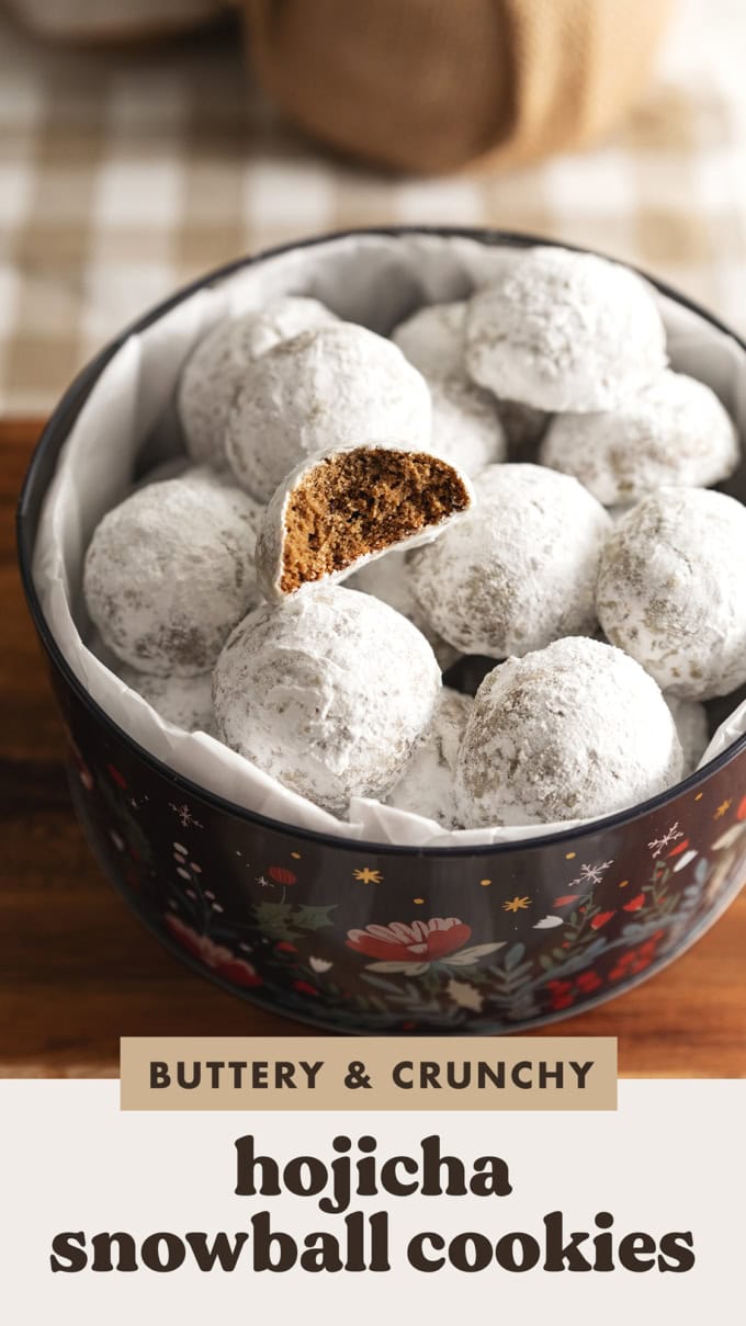 Hojicha snowball cookies in a cookie tin with one cookie on top that has a bite taken out of it to show the texture inside.