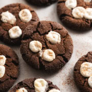 Mexican hot chocolate cookies with marshmallows on top scattered on parchment paper.