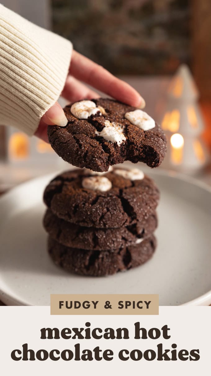 A hand picking up a Mexican hot chocolate cookie with a bite taken out of it with a stack of cookies beneath it.