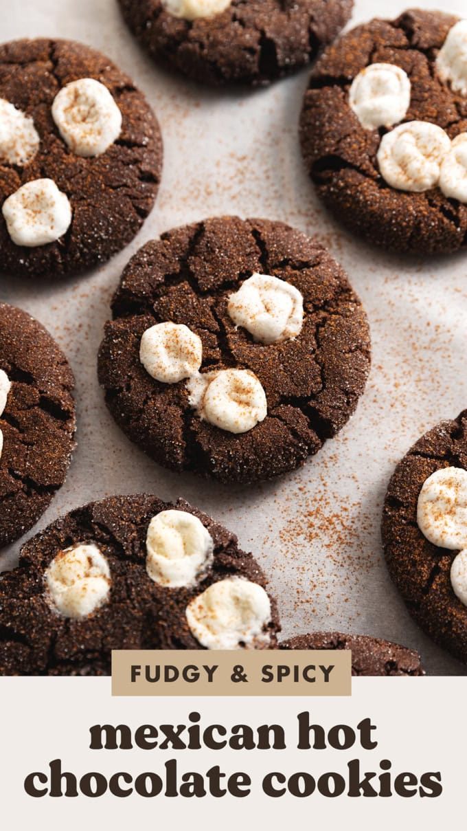 Mexican hot chocolate cookies with marshmallows on top scattered on parchment paper.