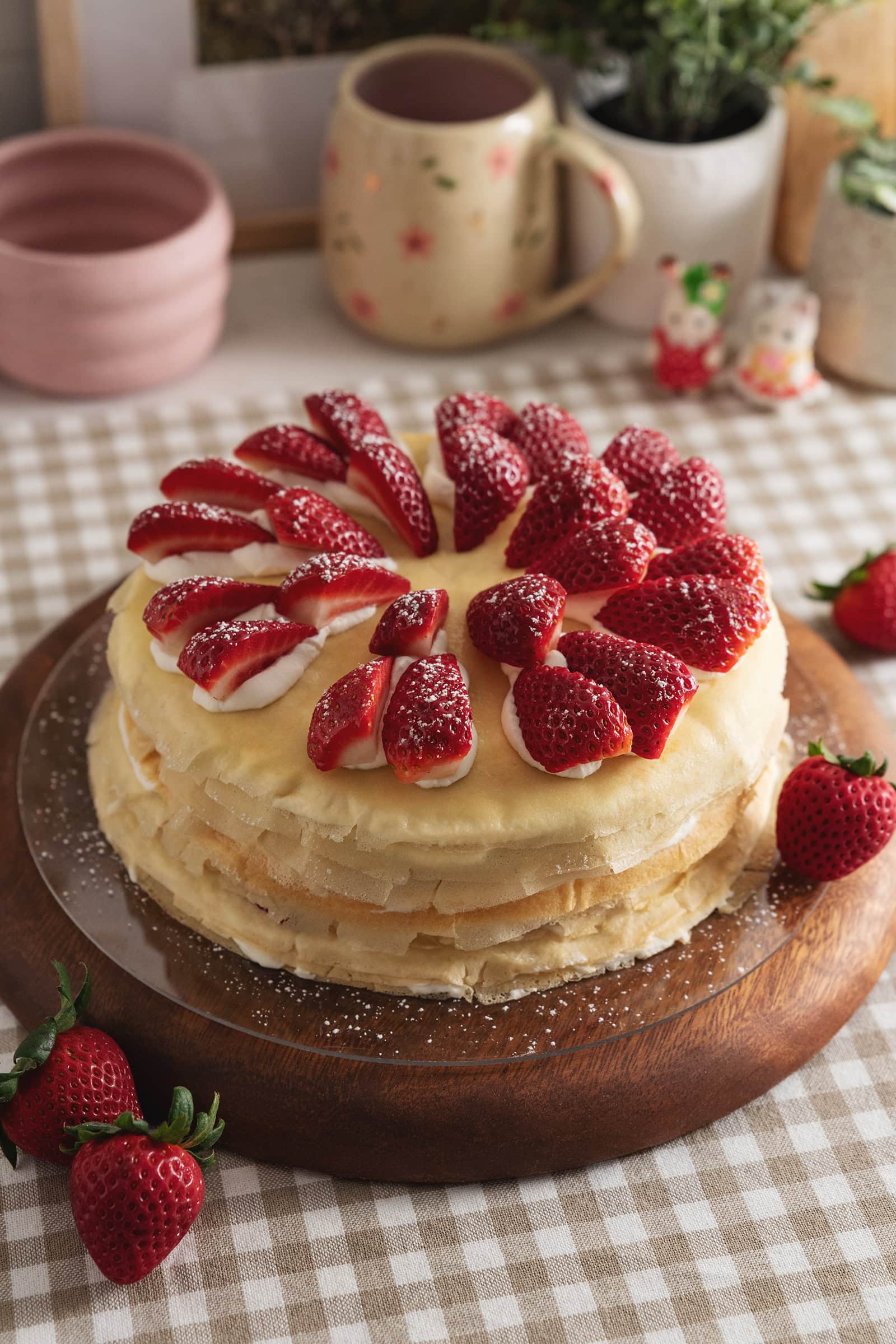 A strawberry crepe cake topped with strawberry slices on a wooden platter.