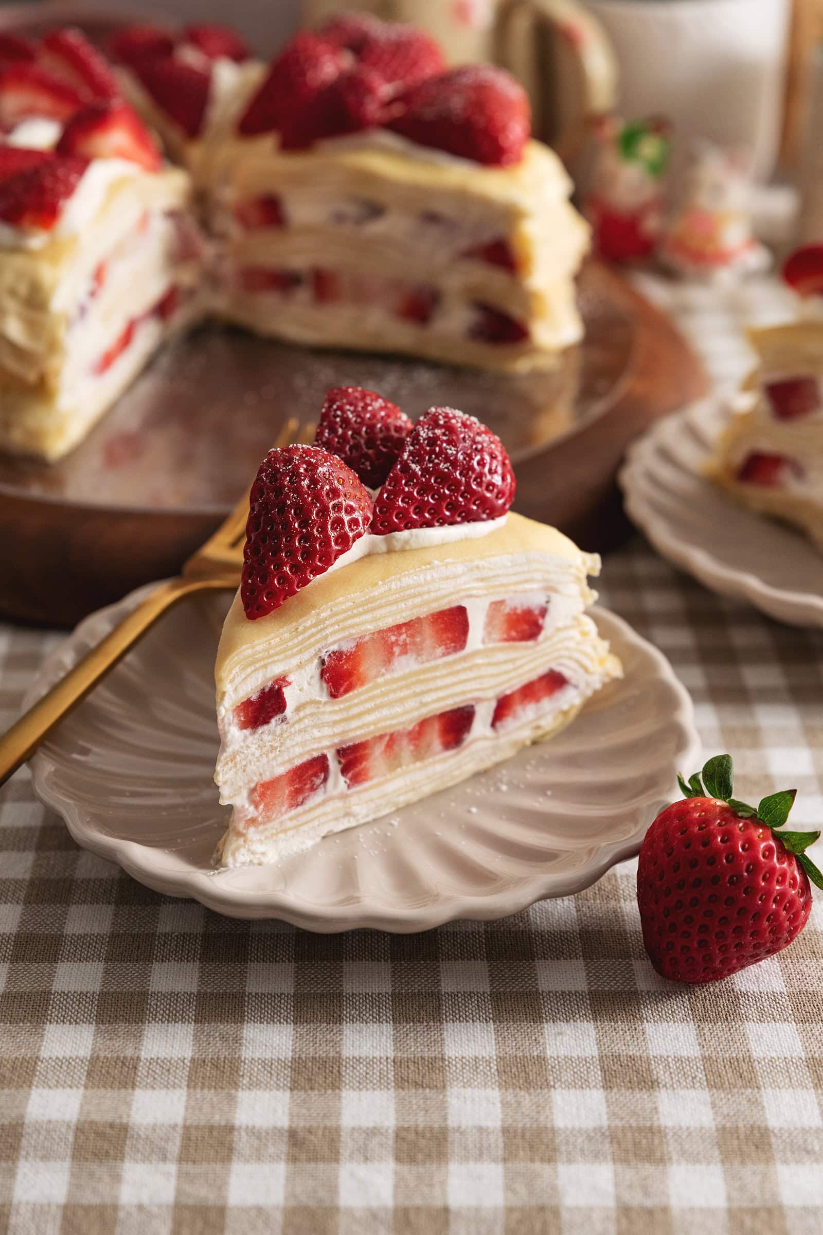 A slice of strawberry crepe cake on a plate with layers of crepes, whipped cream, and strawberry slices.