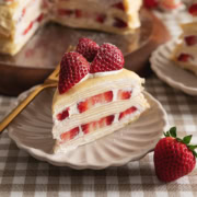 A slice of strawberry crepe cake on a plate with layers of crepes, whipped cream, and strawberry slices.