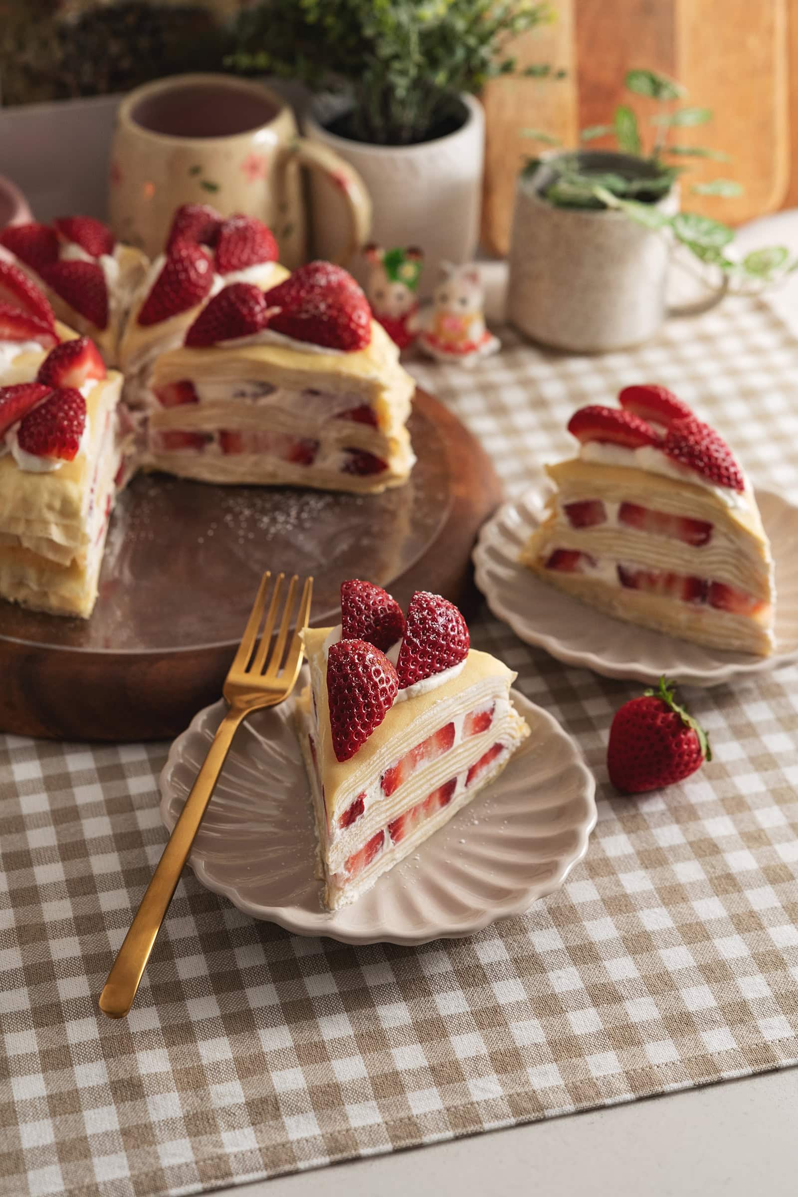 Two slices of strawberry crepe cake on plates in front of the rest of the cake.