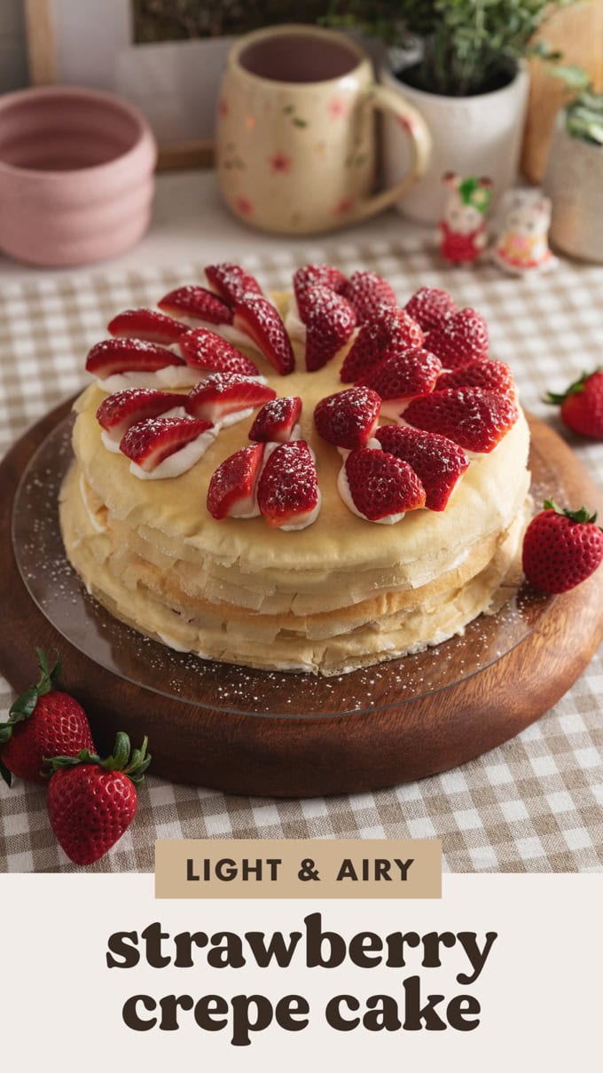 A strawberry crepe cake topped with strawberry slices on a wooden platter.