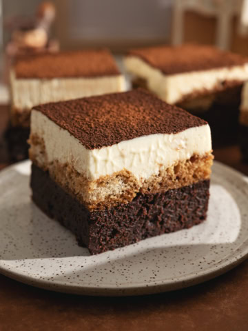 A tiramisu brownie on a speckled plate in front of other brownies.