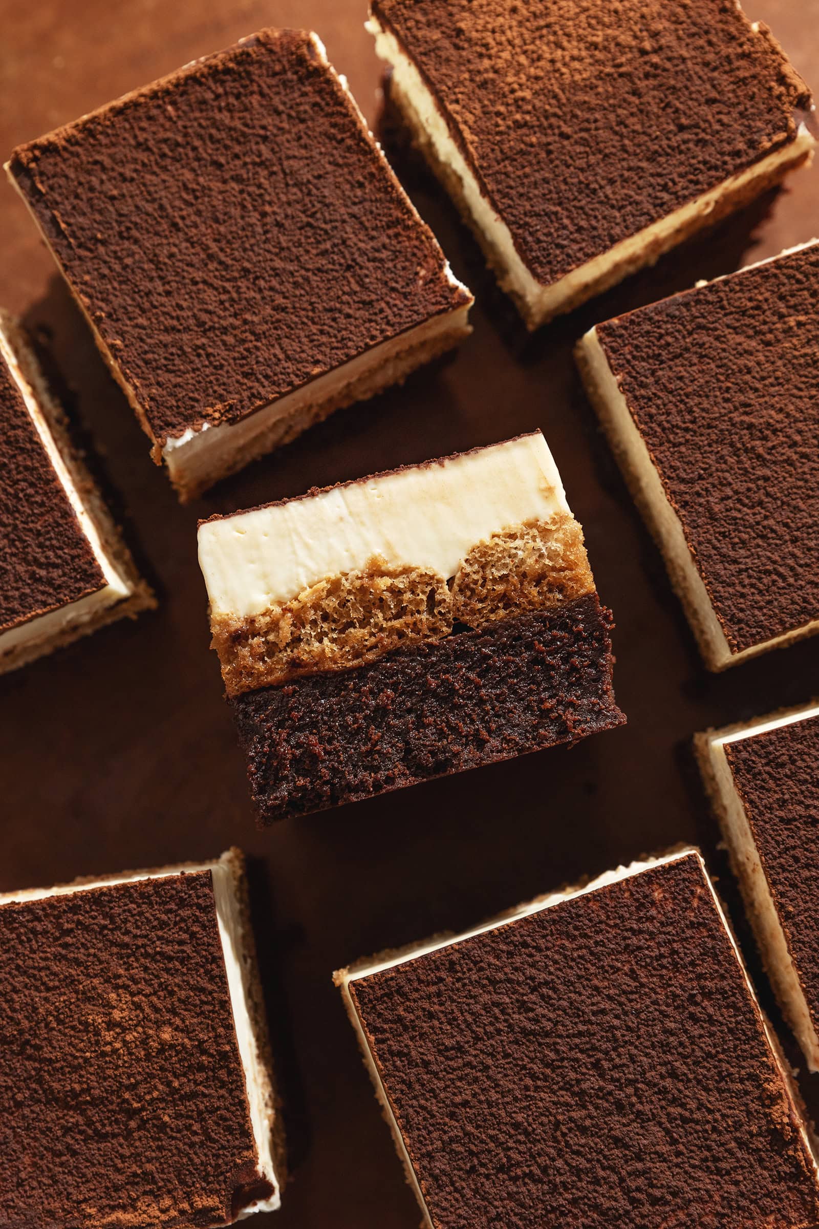 TIramisu brownies scattered on a wooden surface with one brownie laying on its side to show the layers.