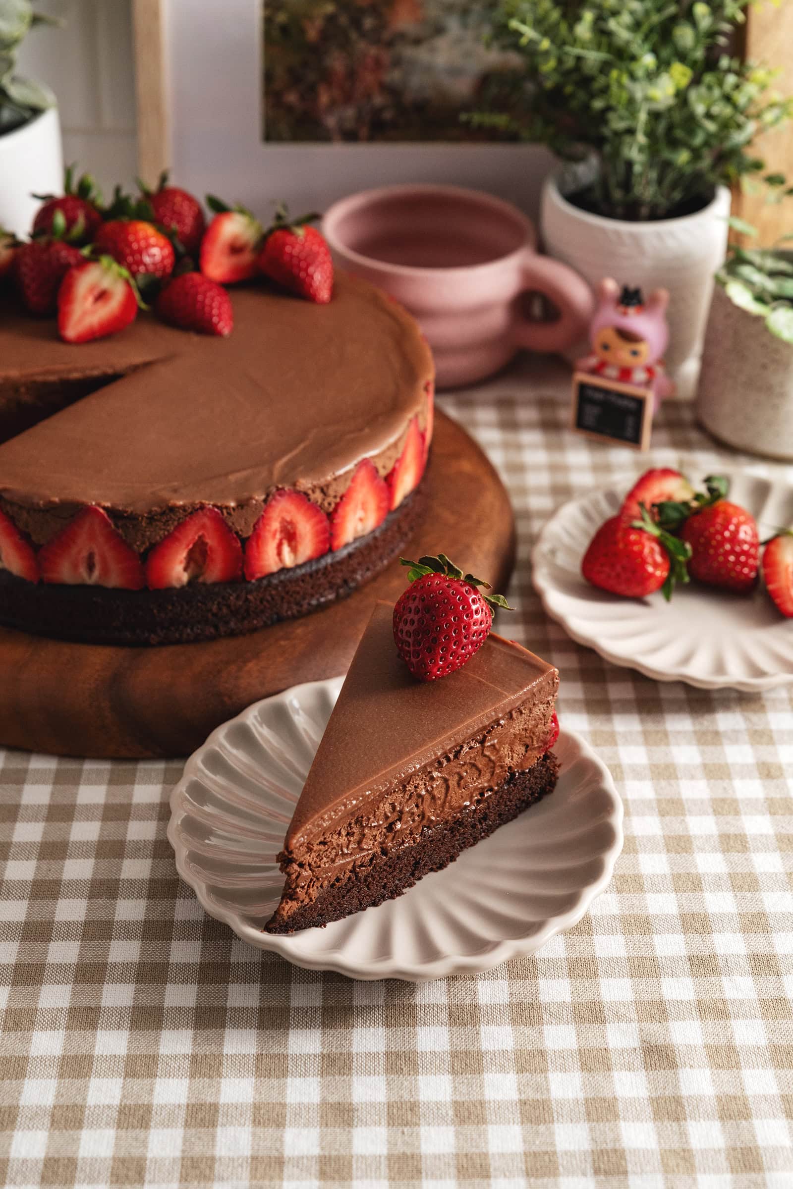 A slice of chocolate mousse cake on a plate in front of the rest of the cake.