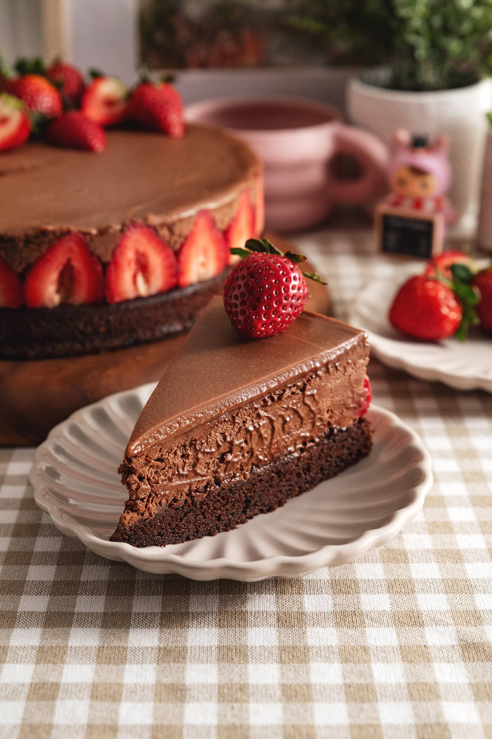 A slice of chocolate mousse cake with a strawberry on top on a plate, showing the three layers of chocolate.