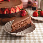 A slice of chocolate mousse cake with a strawberry on top on a plate, showing the three layers of chocolate.