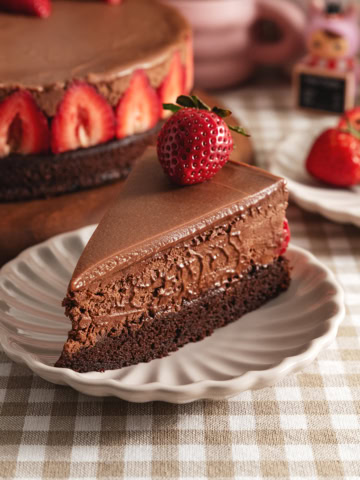 A slice of chocolate mousse cake with a strawberry on top on a plate, showing the three layers of chocolate.
