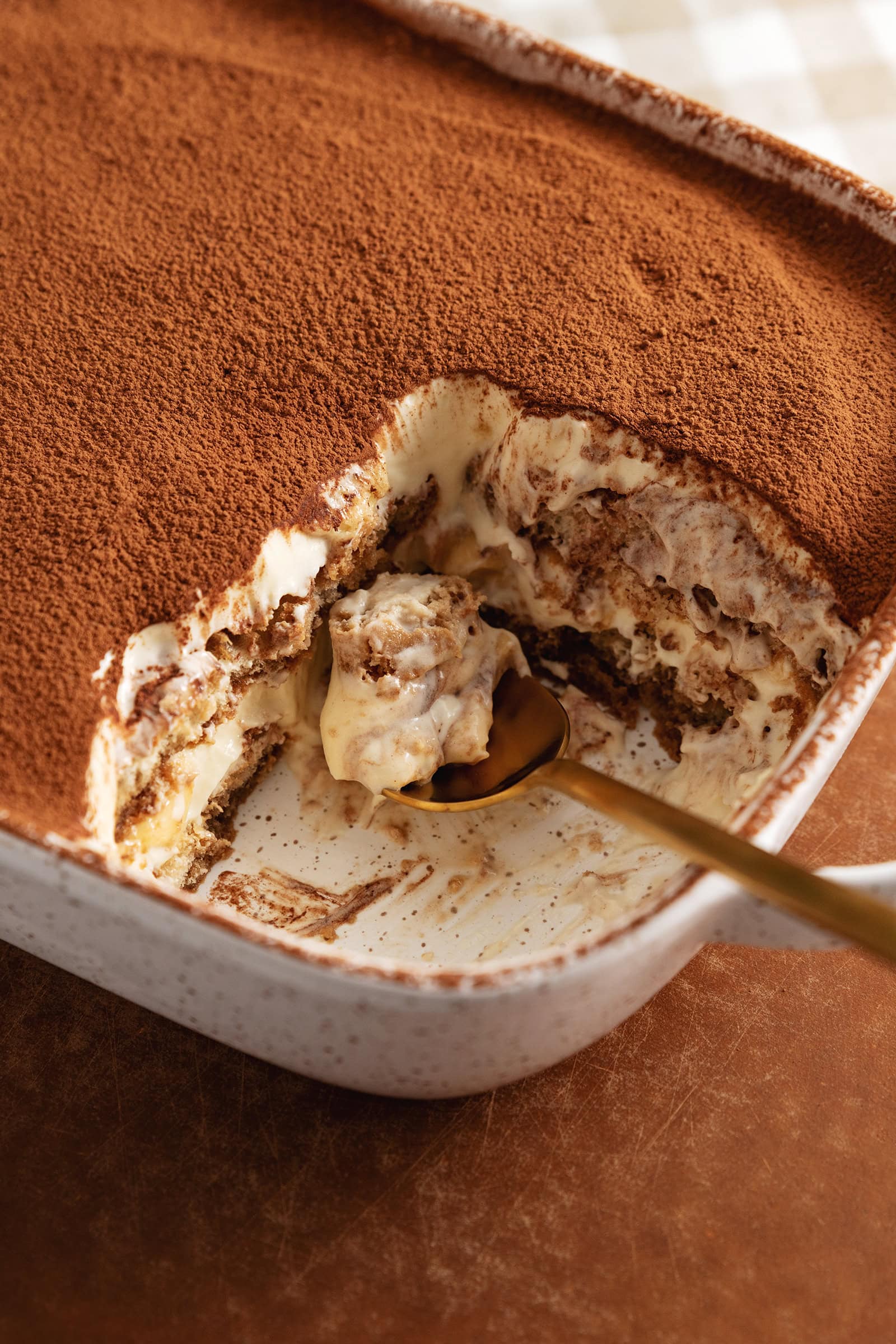 A spoonful of banana pudding tiramisu resting in a dish where the tiramisu was scooped out of.