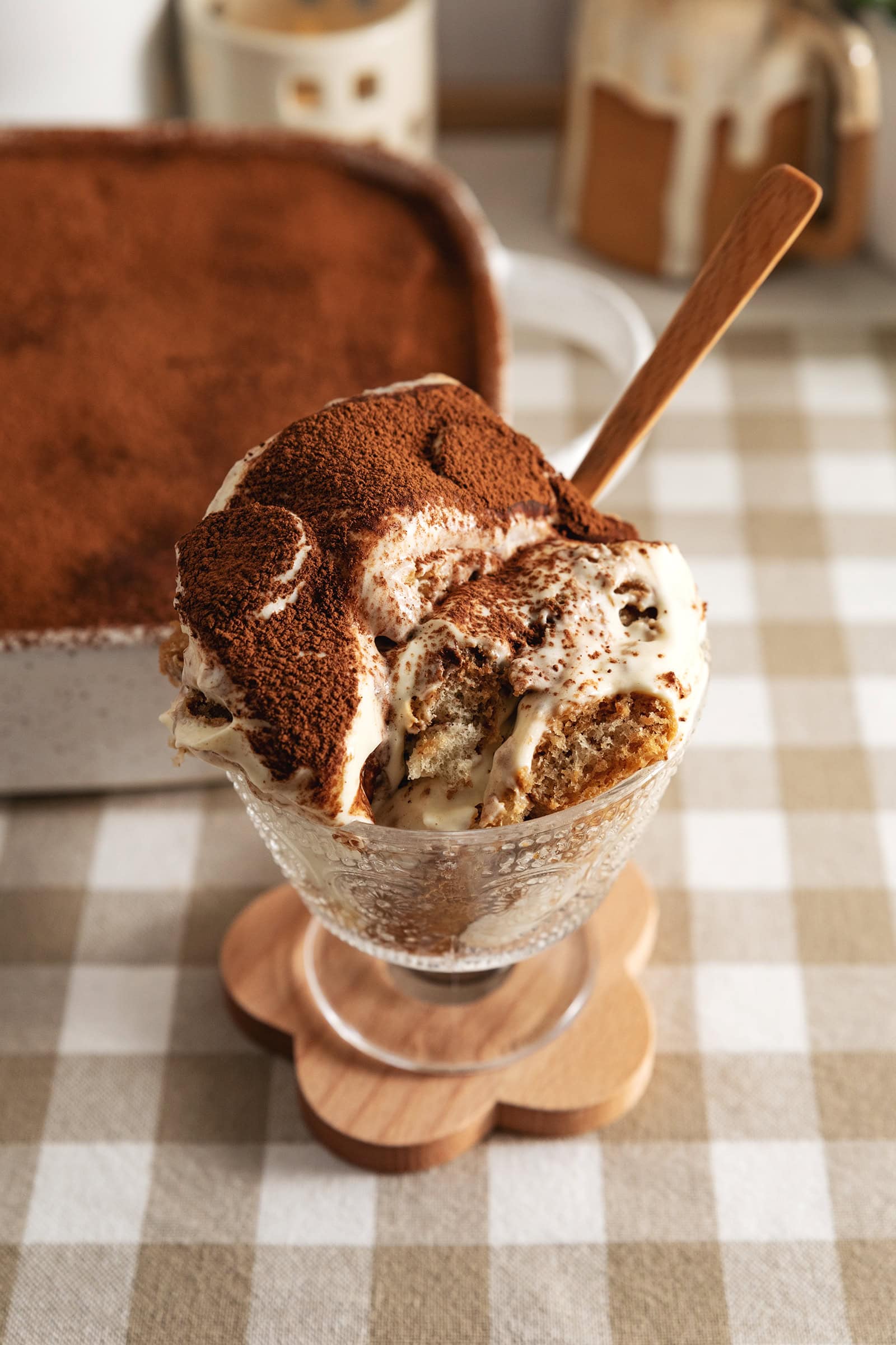A glass serving cup filled with banana pudding tiramisu with a spoon sticking out of it.