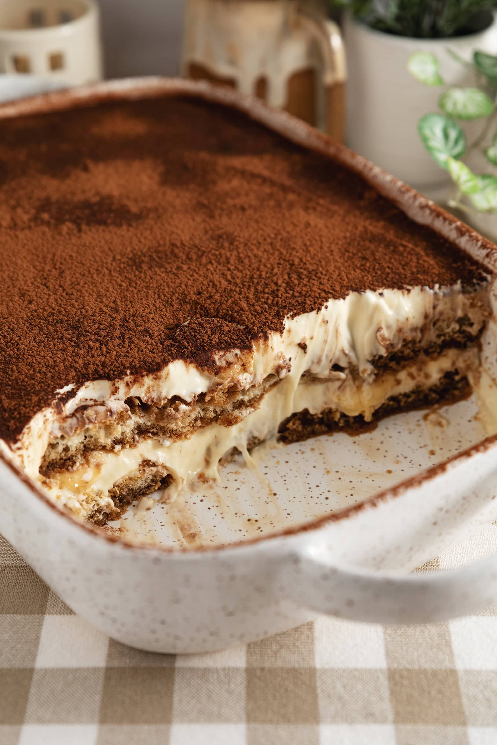 A dish of banana pudding tiramisu with a quarter of it scooped out to show the layers inside.