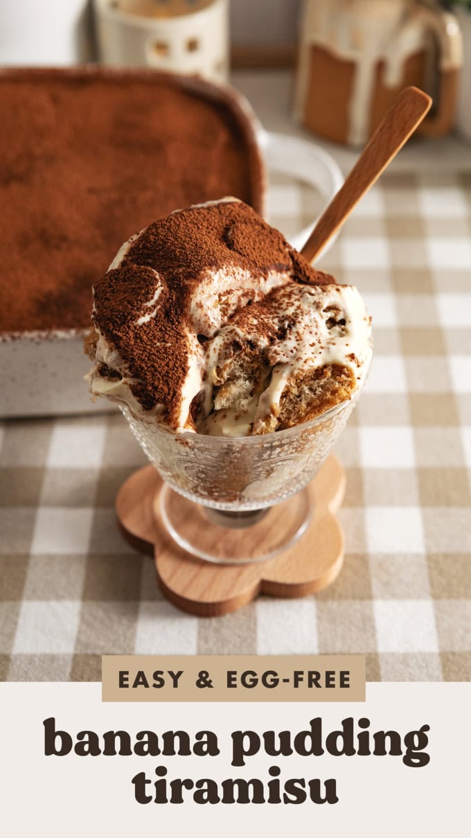 A glass serving cup filled with banana pudding tiramisu with a spoon sticking out of it.