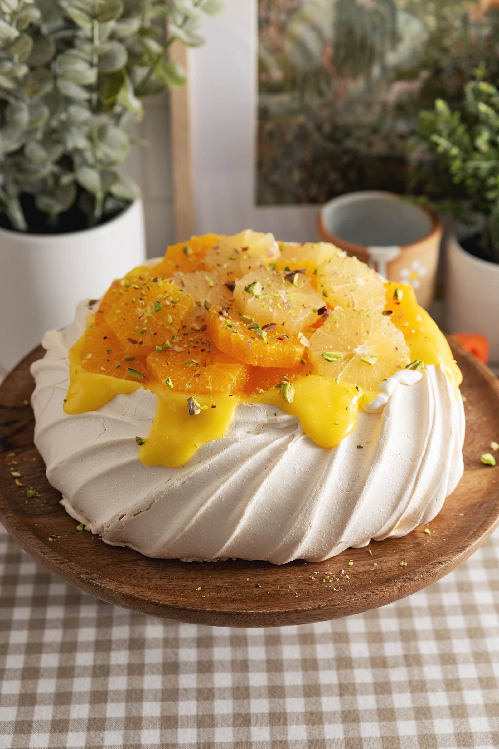 A citrus pavlova on a wooden cake stand.