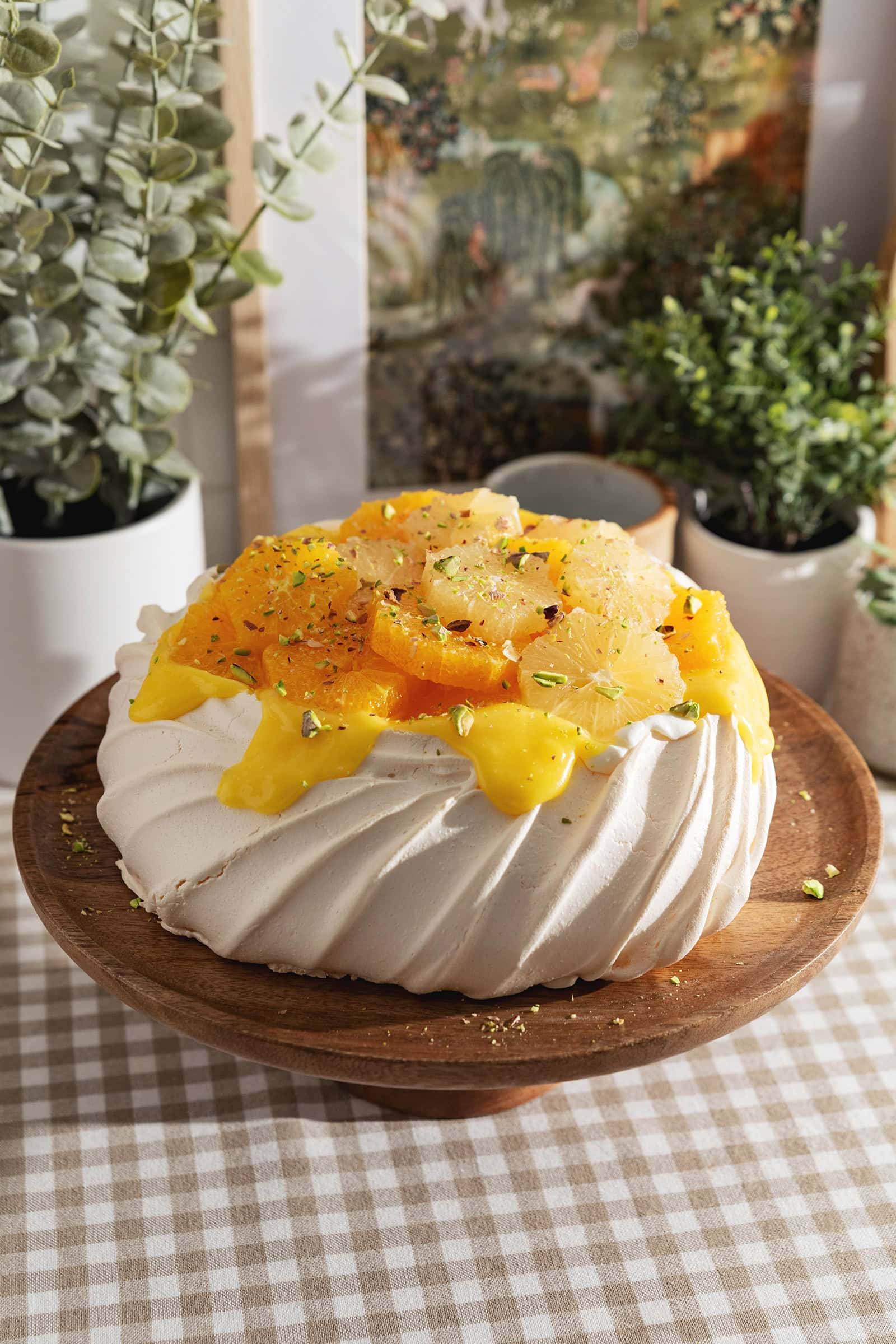 A citrus pavlova on a wooden cake stand.