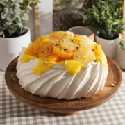 A citrus pavlova sitting on a wooden cake stand.