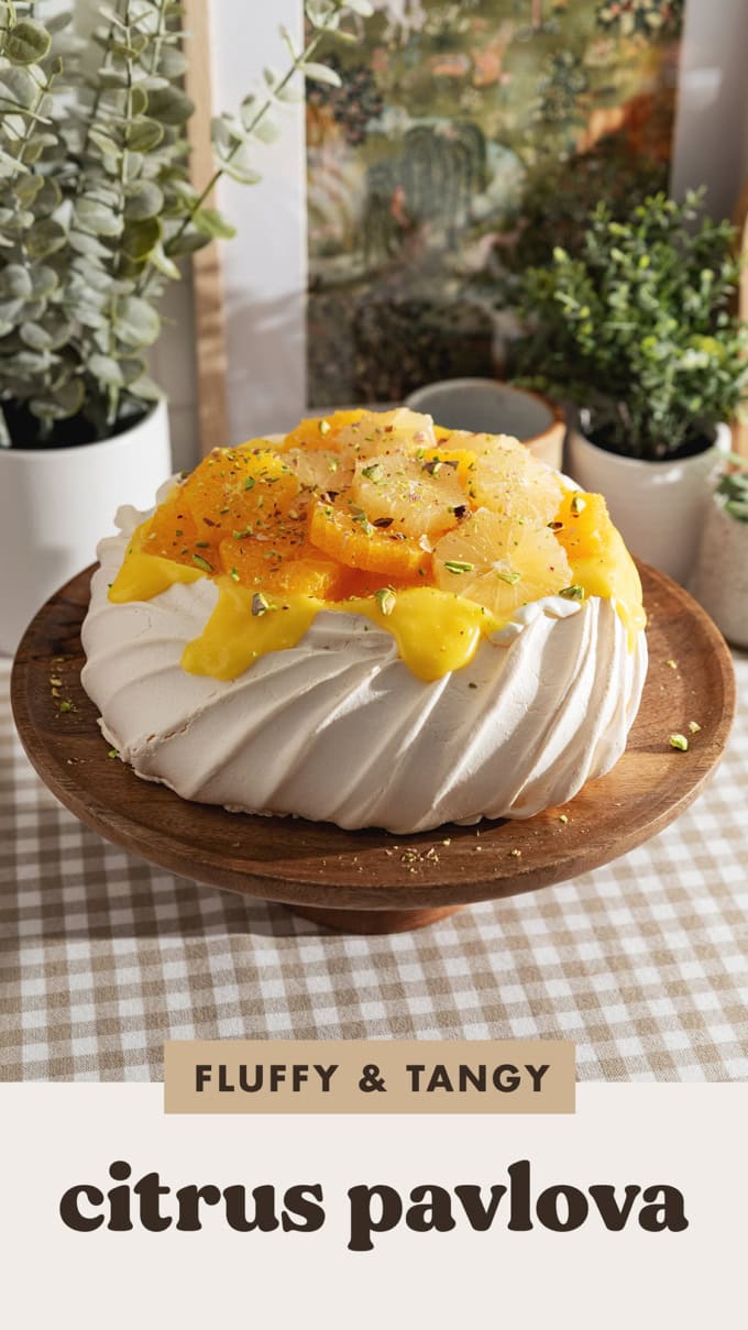 A citrus pavlova on a wooden cake stand.