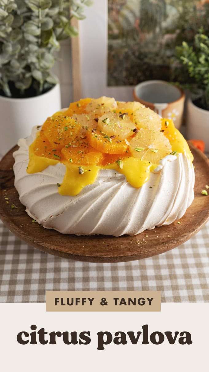 A citrus pavlova on a wooden cake stand.