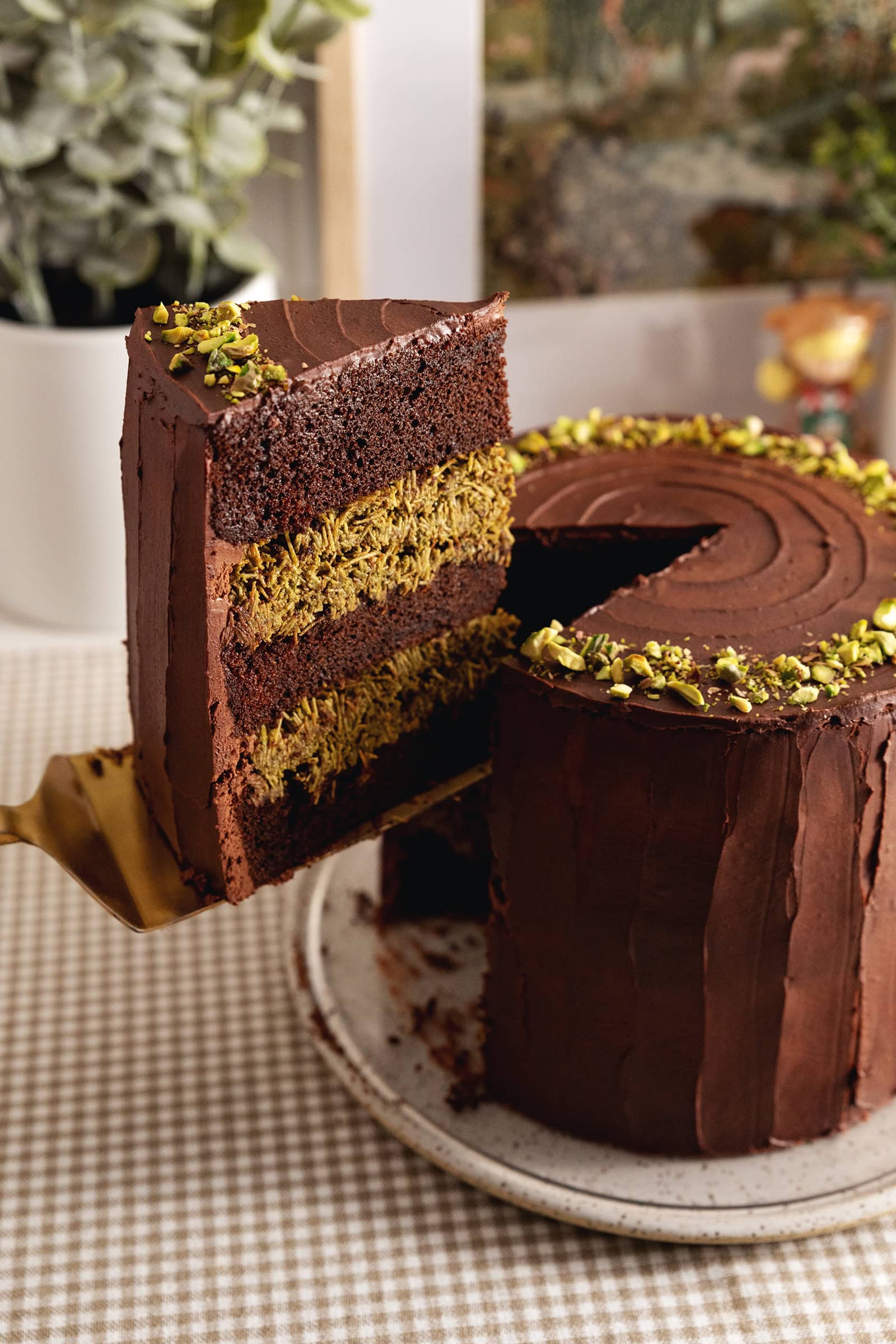 A slice of Dubai chocolate pistachio cake being lifted above the rest of the cake with a cake server.