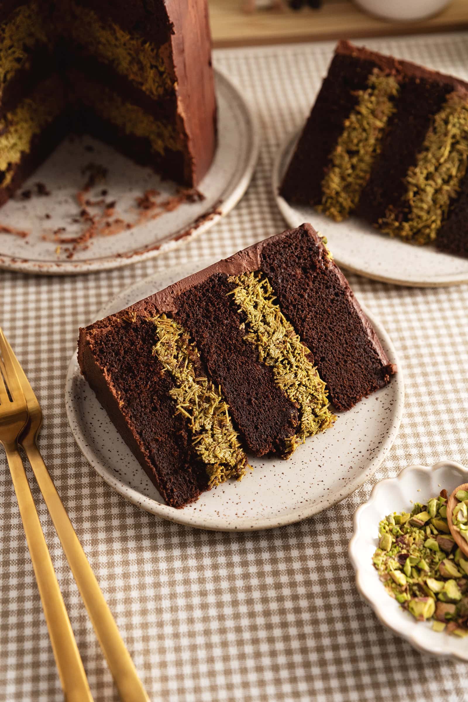 A slice of Dubai chocolate pistachio cake on a speckled plate showing the layers of chocolate cake and pistachio kataifi inside.