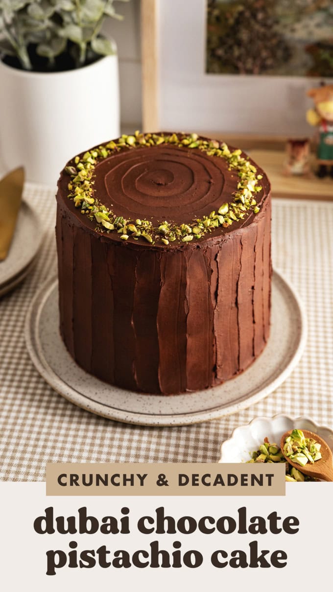 A Dubai chocolate pistachio cake frosted with chocolate ganache and topped with a ring of pistachios on a plate.