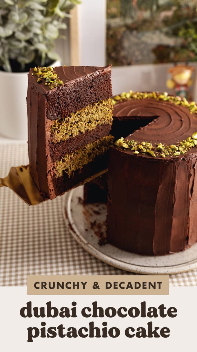 A slice of Dubai chocolate pistachio cake being lifted above the rest of the cake with a cake server.