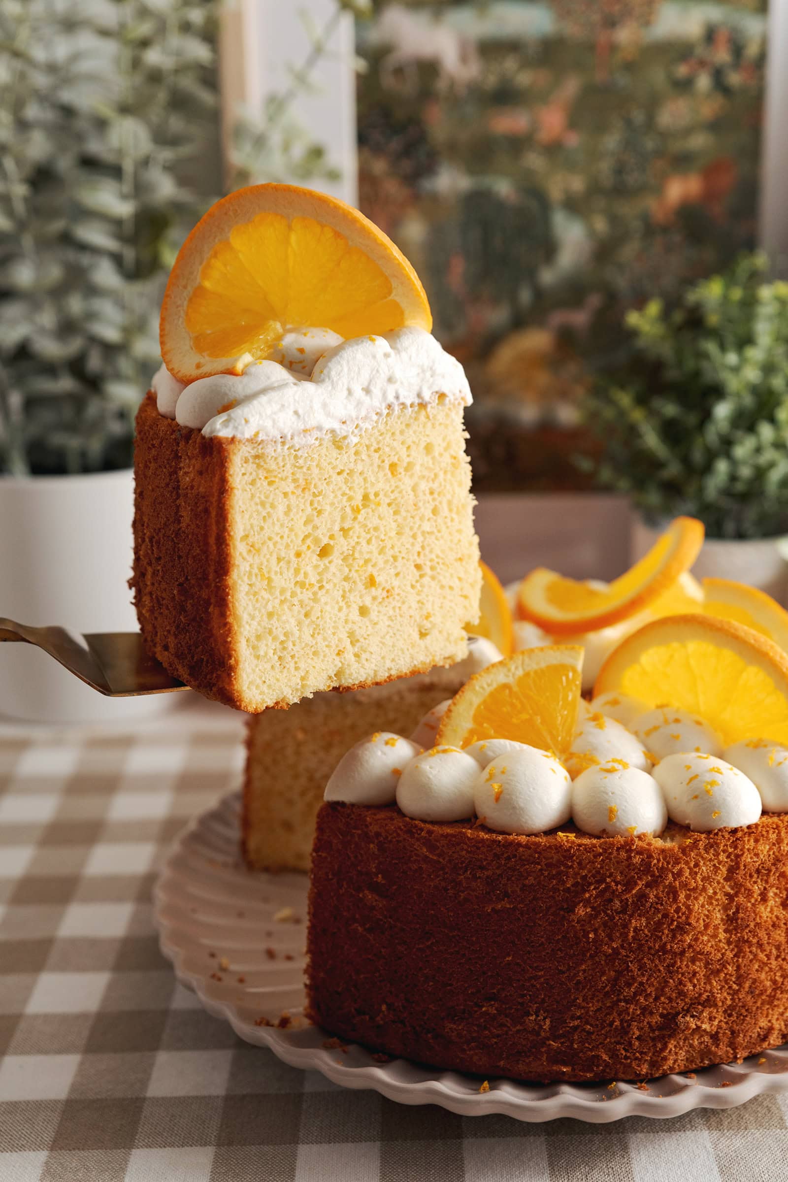 Lifting a slice of orange chiffon cake with a cake server above the rest of the cake.