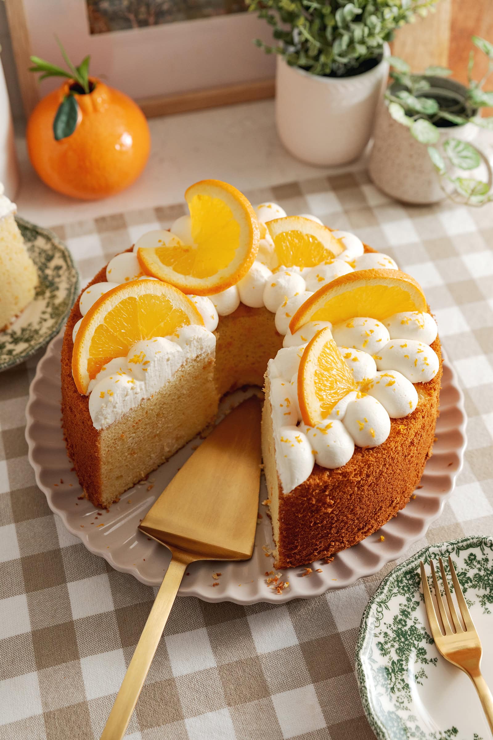 An orange chiffon cake on a plate with a cake server where a slice was removed.
