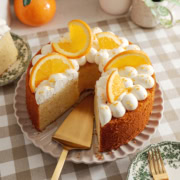 An orange chiffon cake on a plate with a cake server where a slice was removed.