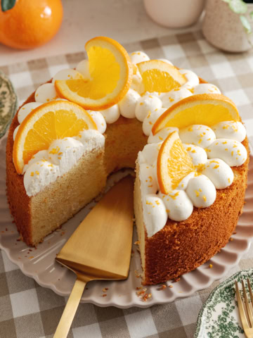 An orange chiffon cake on a plate with a cake server where a slice was removed.