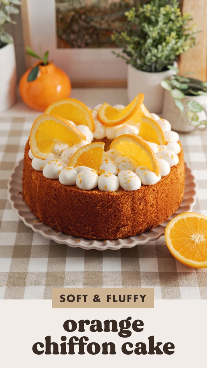 An orange chiffon cake topped with whipped cream blobs and orange slices on a plate.